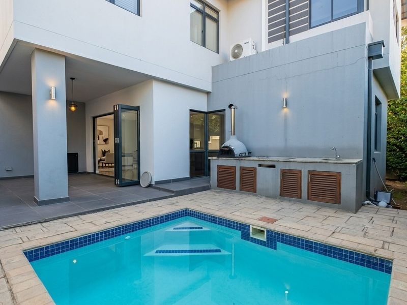 Outdoor entertainment area featuring a swimming pool, paved patio, and a built-in braai station with a pizza oven and sink.