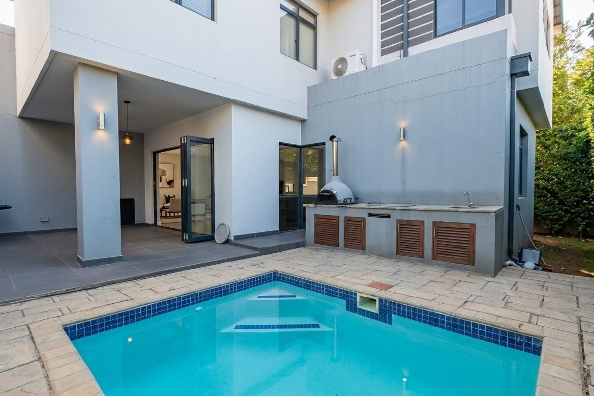 Outdoor entertainment area featuring a swimming pool, paved patio, and a built-in braai station with a pizza oven and sink.