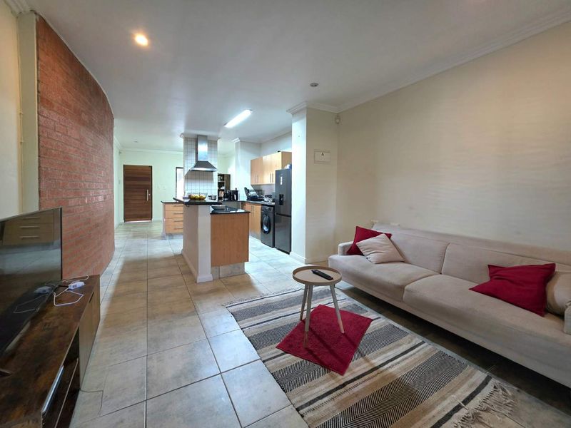 Open-plan living area featuring a distinctive curved exposed brick wall, tiled flooring, and a functional kitchen with built-in cabinetry and a central island.