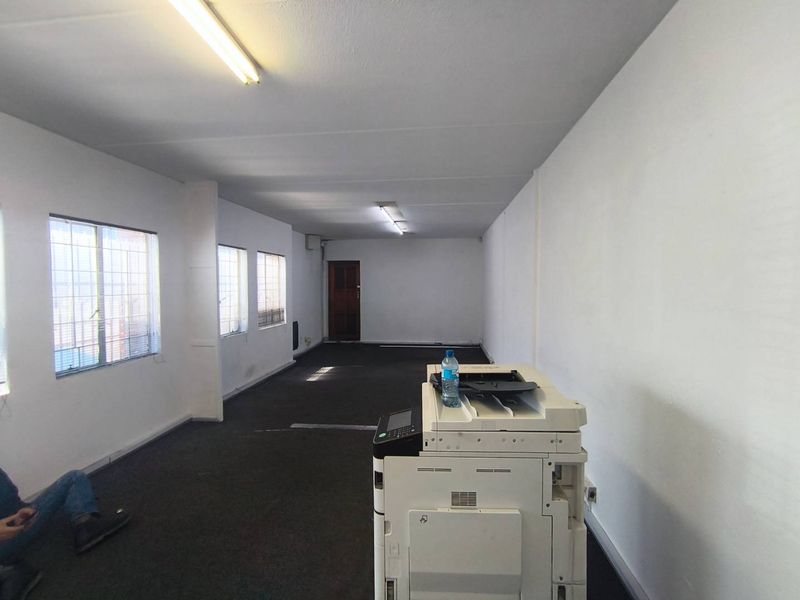 An open-plan office space featuring fluorescent lighting, security-barred windows, and carpeted flooring, suitable for a functional workspace.