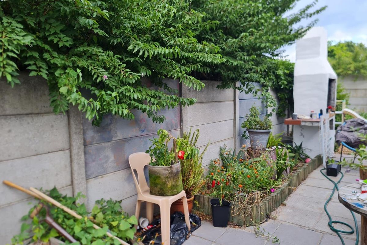 A rear garden area featuring a paved patio, a built-in outdoor fireplace, and a concrete boundary wall with established greenery.