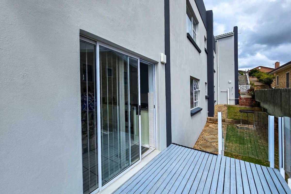 A rear view of the property featuring a timber deck, sliding glass doors, and a small landscaped garden area.