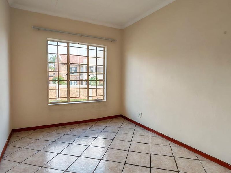 An empty bedroom featuring neutral wall paint, tiled flooring, and a grid-pattern window with an installed curtain rail.