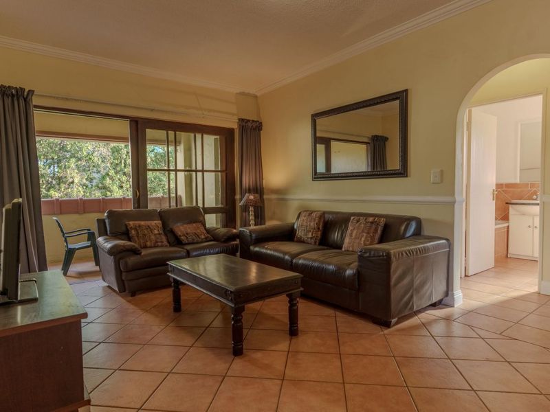 Spacious living room featuring terracotta floor tiles, crown molding, and an arched doorway leading to an adjacent room, with access to a balcony.