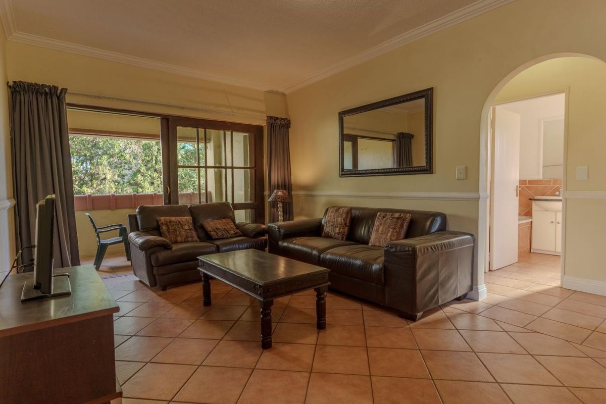Spacious living room featuring terracotta floor tiles, crown molding, and an arched doorway leading to an adjacent room, with access to a balcony.