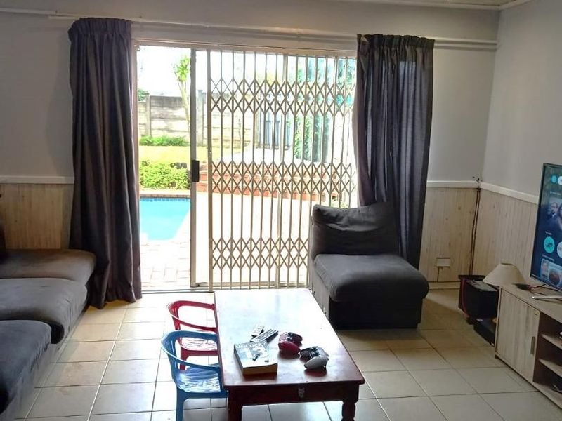 Spacious living room featuring tiled floors, timber ceiling paneling, and a sliding door with security gate providing direct access to the pool area.