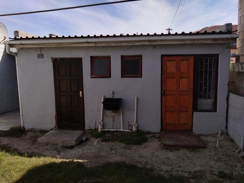 Rear exterior view of an outbuilding featuring two entry doors, small windows with security bars, and an external utility sink.