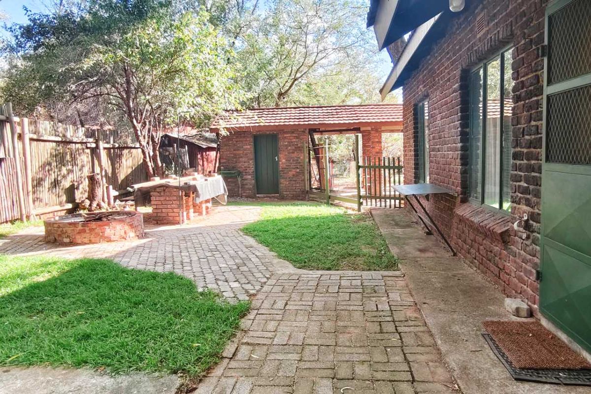 A private rear garden featuring a brick-paved patio area, built-in fire pit, and established trees, providing a functional outdoor space for relaxation.