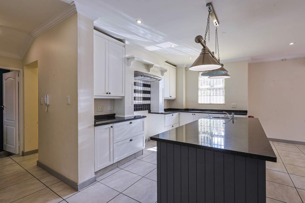 Modern kitchen featuring a central island with granite countertops, white cabinetry, tiled flooring, and integrated extractor fan.