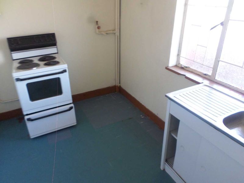 A basic, dated kitchen area featuring a freestanding stove, a single sink unit, and a window with security bars.