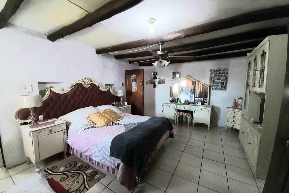 Spacious bedroom featuring exposed timber ceiling beams, tiled flooring, and a ceiling fan.