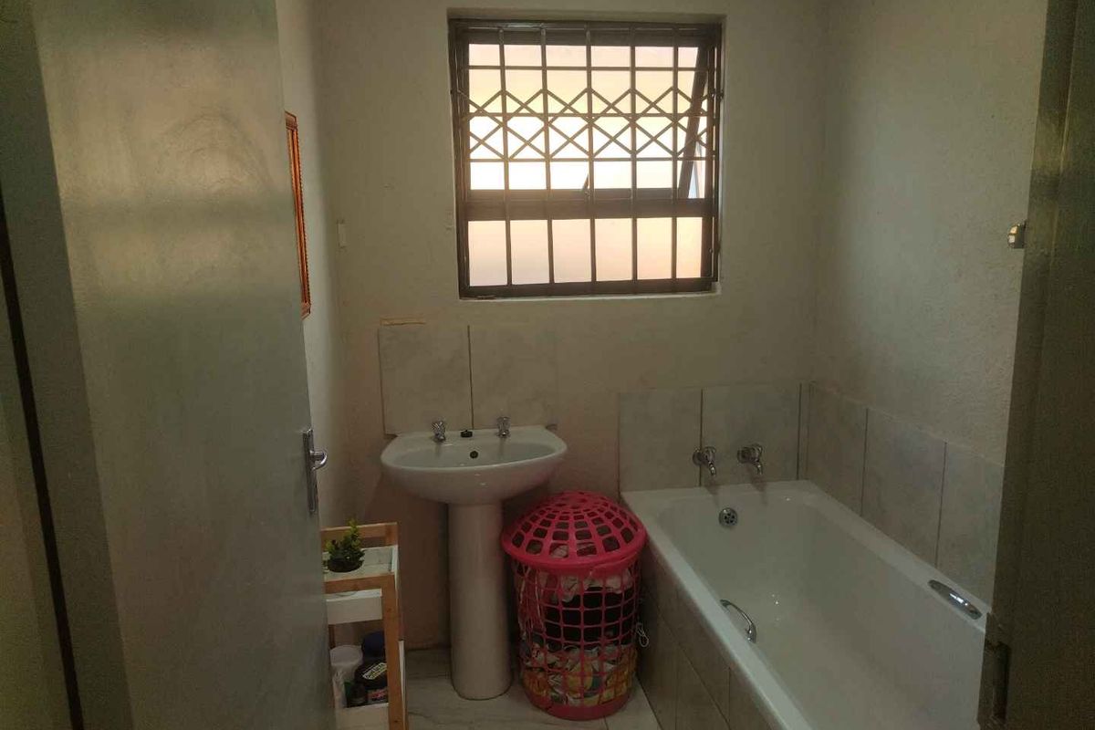 A functional bathroom featuring a standard bathtub, pedestal basin, and a window with security bars.