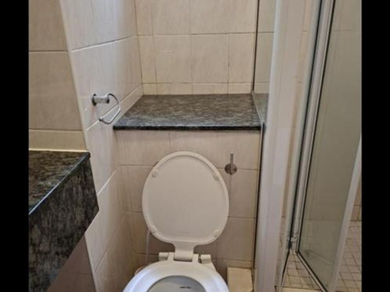 A functional bathroom featuring a toilet, shower enclosure, and granite vanity surfaces with neutral wall tiling.