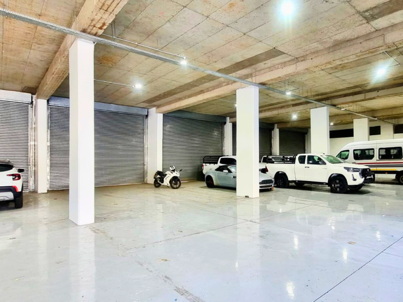 Spacious industrial garage featuring high concrete ceilings, durable epoxy flooring, and multiple roller shutter doors for easy vehicle access.