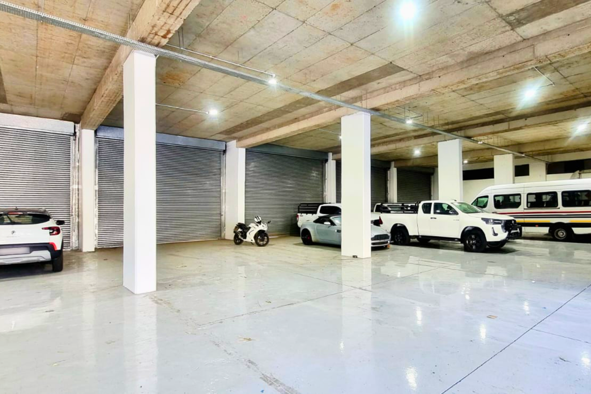 Spacious industrial garage featuring high concrete ceilings, durable epoxy flooring, and multiple roller shutter doors for easy vehicle access.