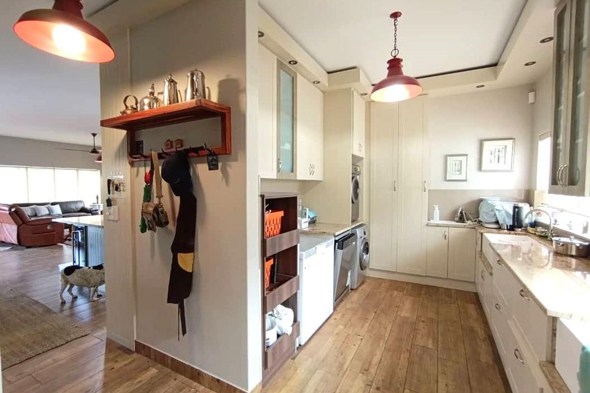 A functional kitchen featuring light-toned cabinetry, stone countertops, a farmhouse-style sink, and integrated laundry appliances, seamlessly flowing into the adjacent living area.