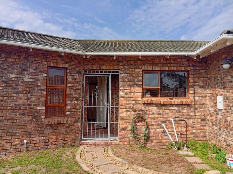 Rear exterior view of a face brick house featuring a tiled roof, timber window frames, and a security gate entrance.