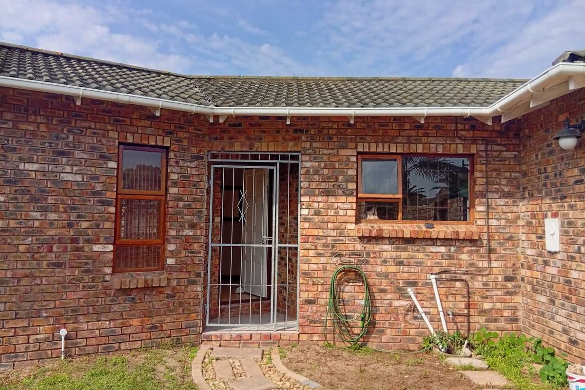 Rear exterior view of a face brick house featuring a tiled roof, timber window frames, and a security gate entrance.