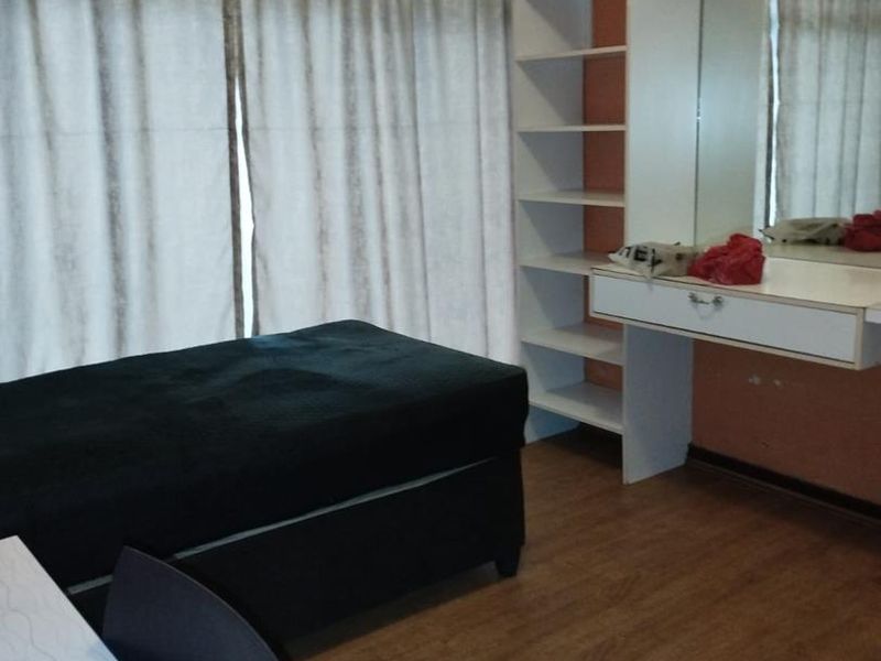 A bedroom featuring laminate flooring, built-in shelving, and a wall-mounted vanity unit with a mirror.