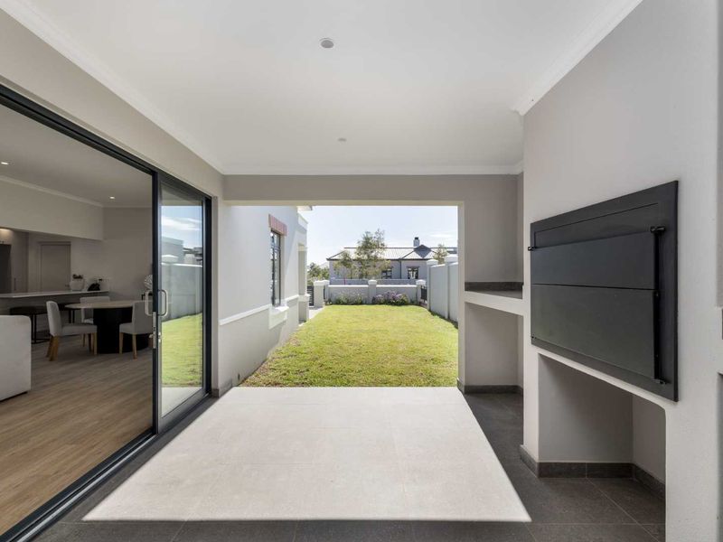 Covered patio featuring a built-in braai, tiled flooring, and large sliding doors providing seamless access to the rear garden.