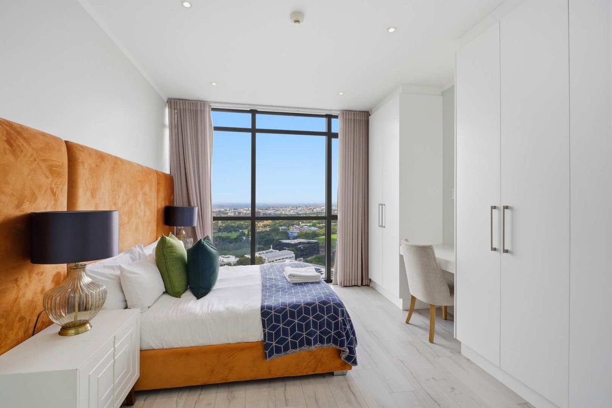 Modern bedroom featuring floor-to-ceiling windows with expansive city views, built-in white cabinetry, and recessed ceiling lighting.