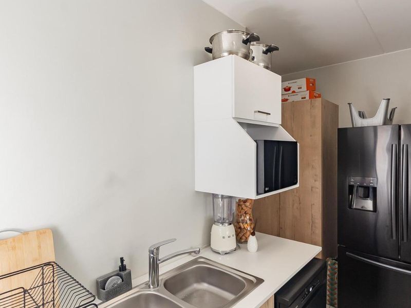 A functional kitchen area featuring a stainless steel double sink, chrome mixer tap, and white wall-mounted cabinetry with integrated microwave housing.