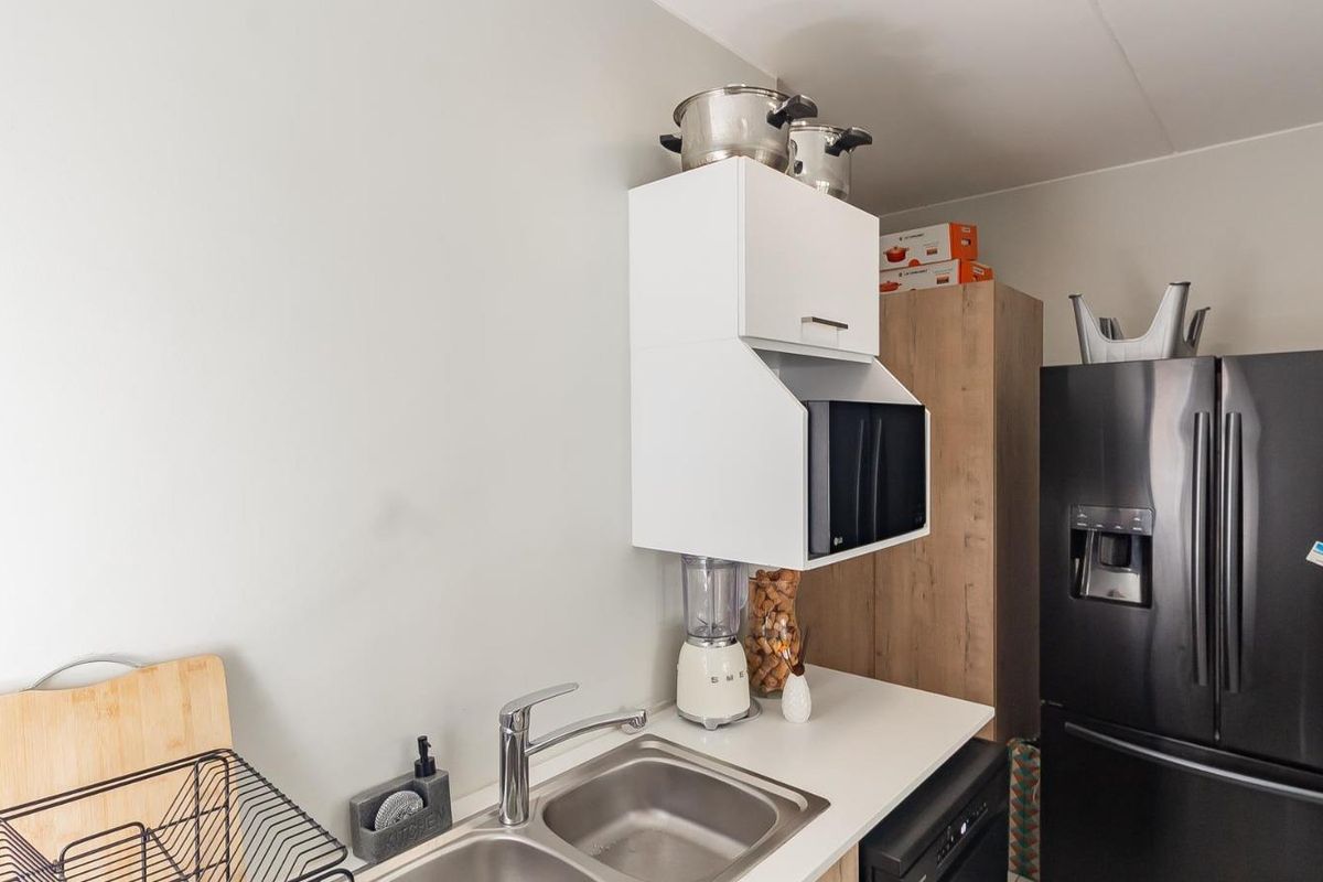A functional kitchen area featuring a stainless steel double sink, chrome mixer tap, and white wall-mounted cabinetry with integrated microwave housing.