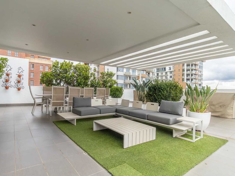 Spacious covered penthouse balcony featuring tiled flooring, recessed lighting, and a modern slatted pergola, offering an ideal outdoor entertainment area.
