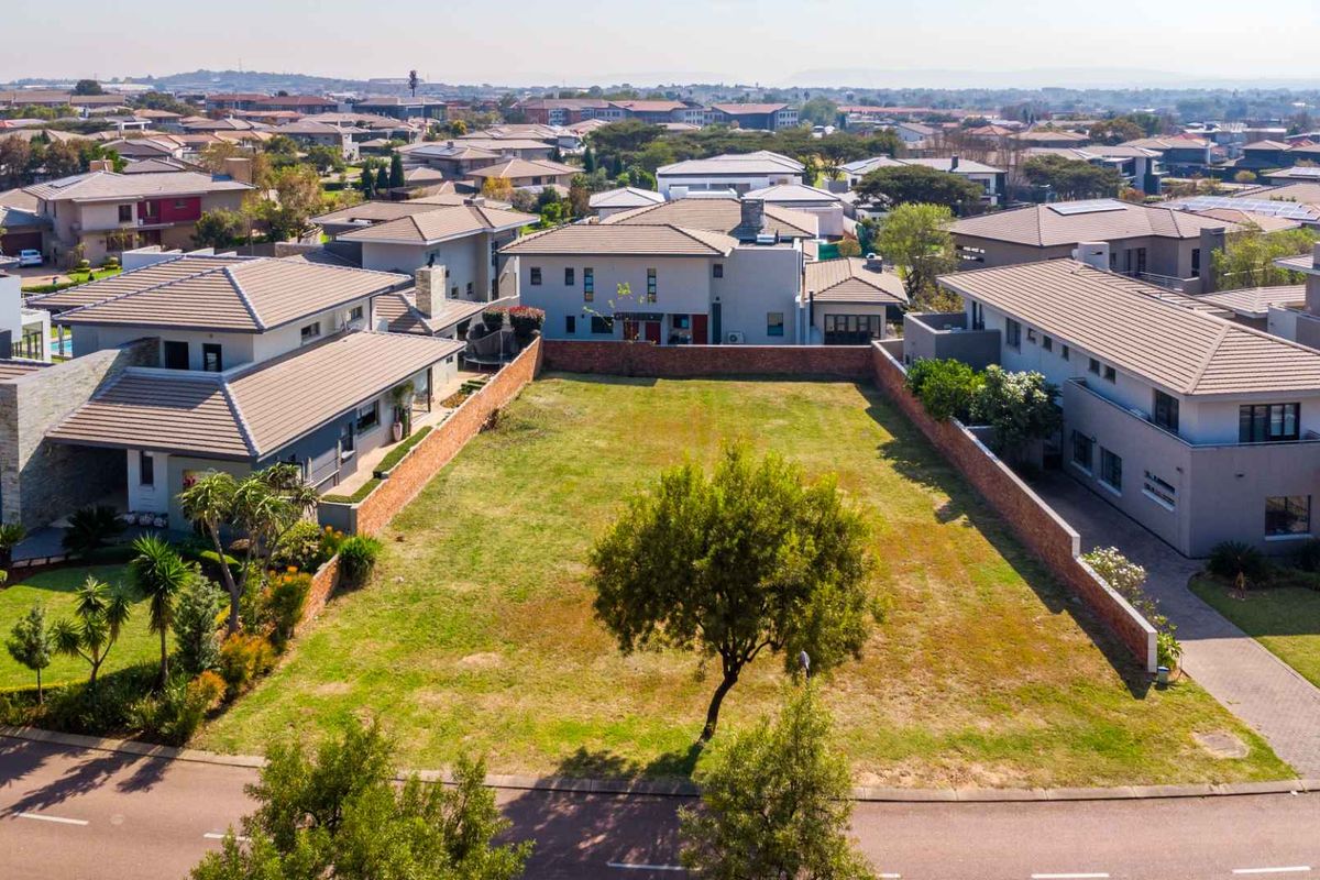 An elevated aerial view of a vacant residential plot situated within a developed estate, featuring established boundary walls and surrounding modern homes.
