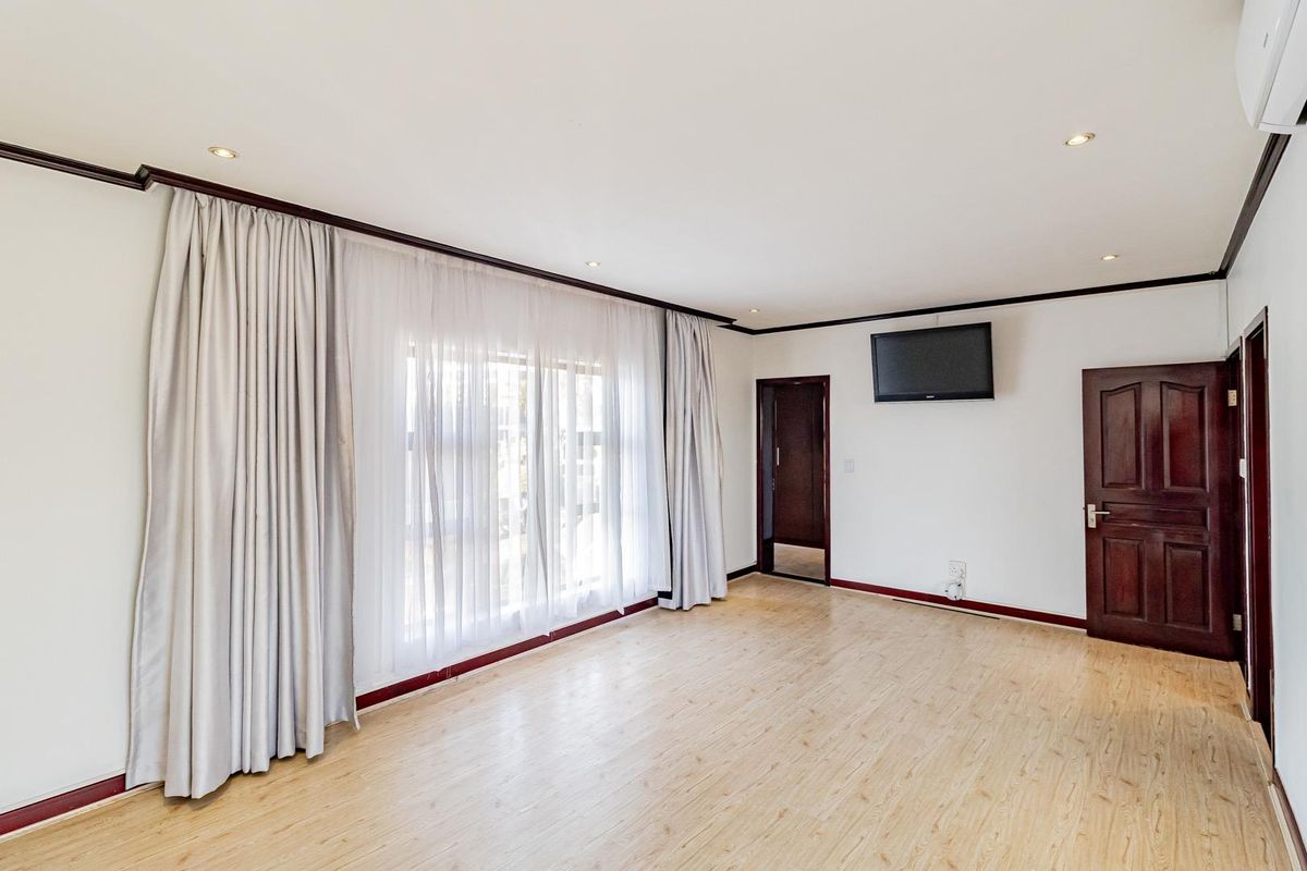 A spacious bedroom featuring light wood-look flooring, recessed ceiling lighting, and a dark wood door, offering a clean and neutral living space.