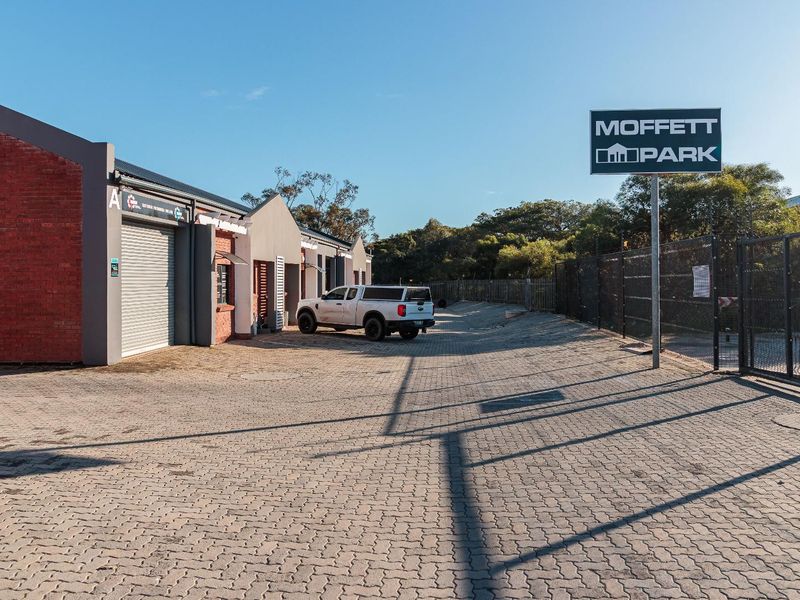 Front view of Moffett Park commercial property featuring paved driveway, brick facade buildings with roller shutter doors, and perimeter security fencing.