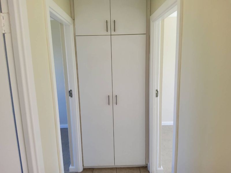 A functional hallway featuring built-in floor-to-ceiling storage cabinetry and neutral tiled flooring, providing efficient access between adjacent rooms.