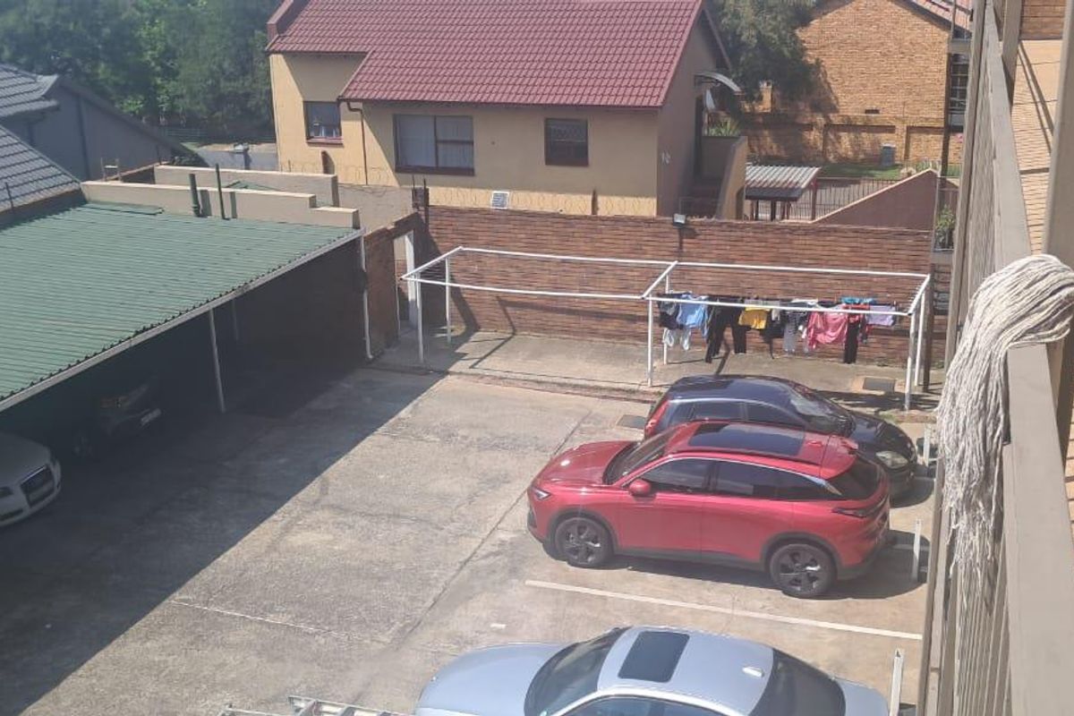 Elevated view overlooking the apartment complex parking area, featuring a covered carport structure and a paved courtyard with a communal drying rack.
