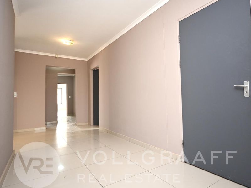 A clean, empty hallway featuring neutral wall tones, tiled flooring, and modern internal doors, providing a bright and functional transition space.