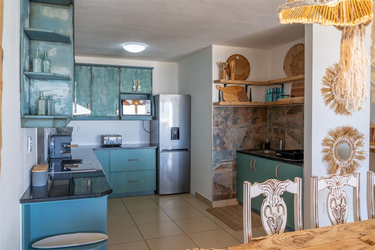 A functional kitchen featuring teal cabinetry, dark countertops, a stone-tiled backsplash, and integrated shelving, providing a practical workspace within the open-plan living area.