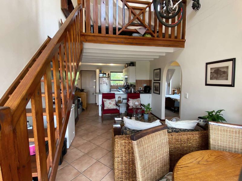 Open plan living area featuring a wooden staircase leading to a mezzanine level, tiled flooring, and an arched entryway to the bedroom.