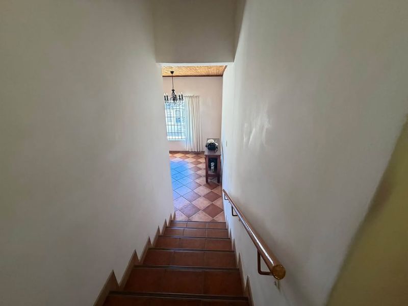 A staircase with tiled steps and a wooden handrail leading down to a tiled landing area with a window.