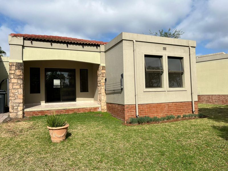 Rear view of the cluster home featuring a covered patio, stone and brick detailing, and a small private garden area.