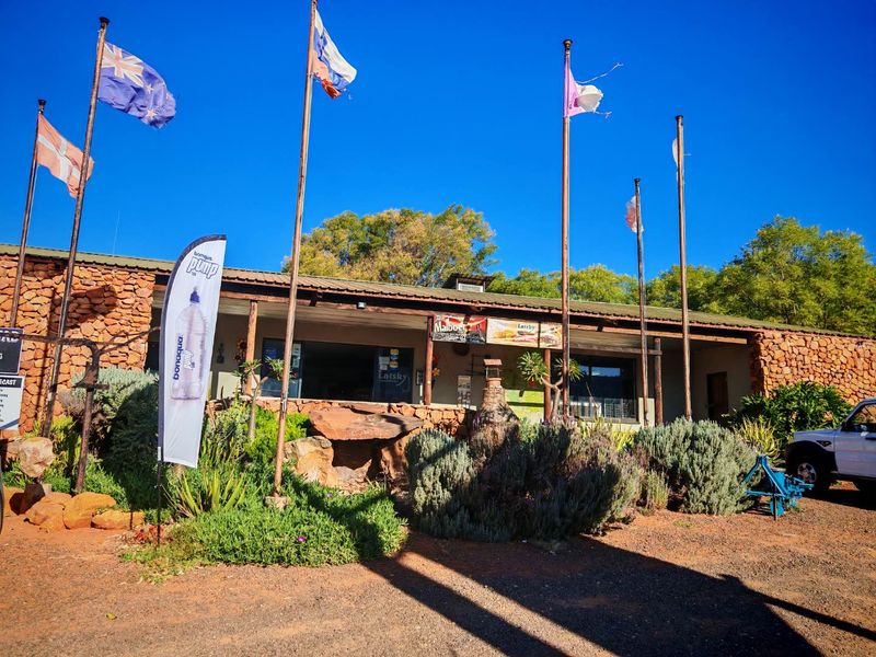 Front elevation of a mixed-use property featuring stone cladding, a covered veranda, and multiple flagpoles in a rural setting.