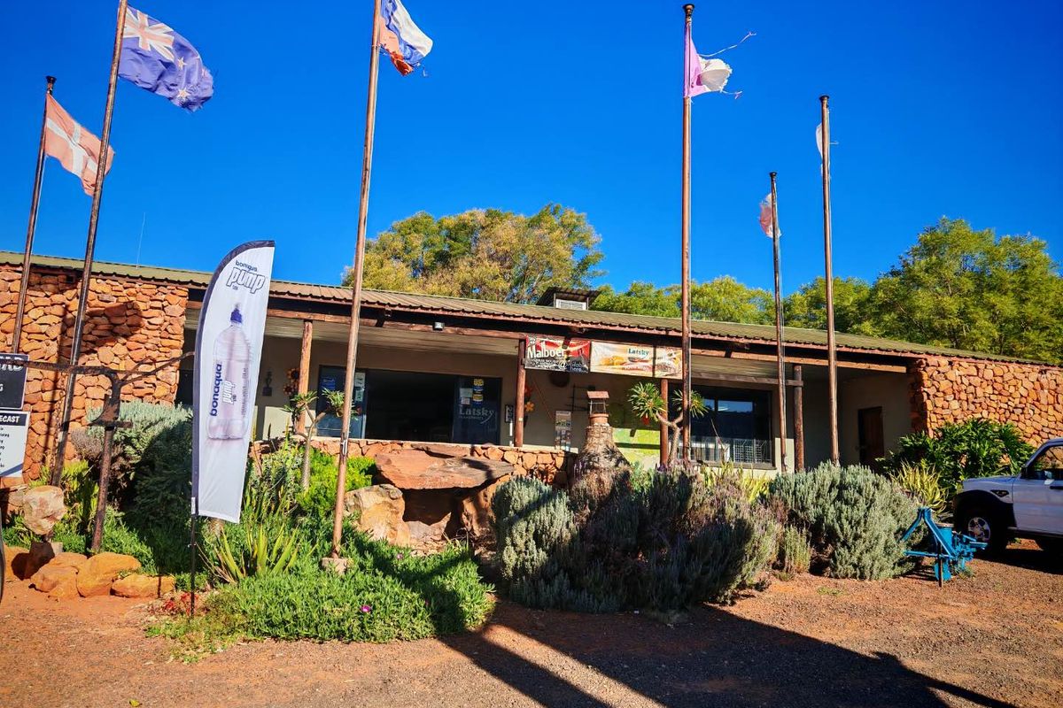 Front elevation of a mixed-use property featuring stone cladding, a covered veranda, and multiple flagpoles in a rural setting.