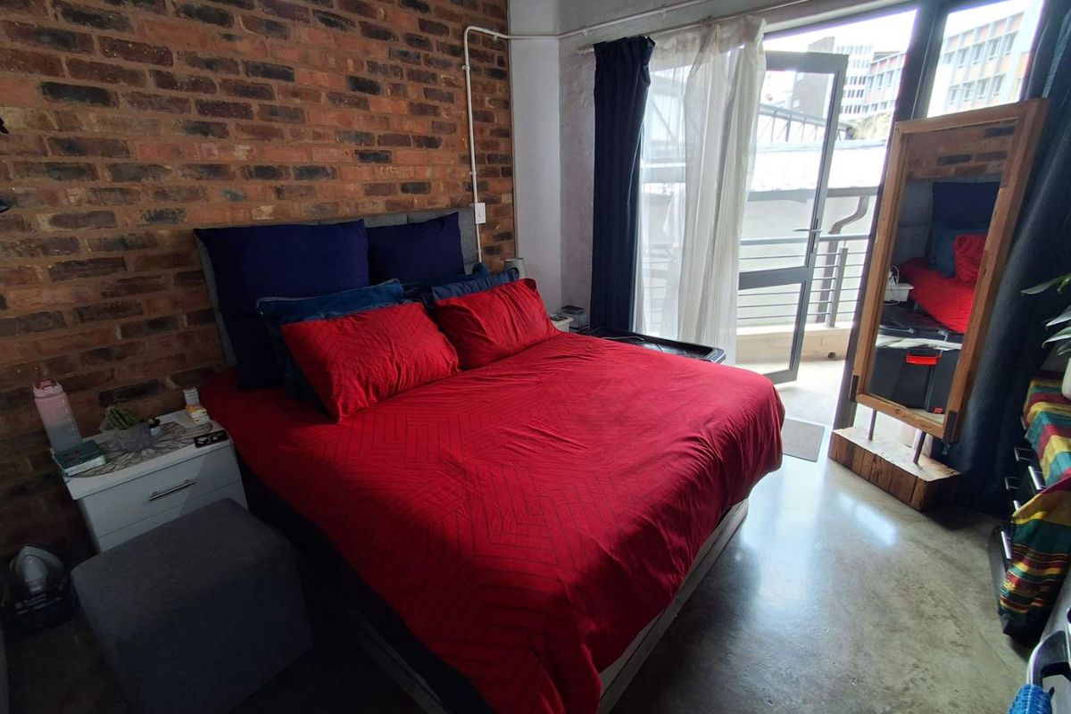 A bedroom featuring an exposed brick feature wall, polished concrete flooring, and direct access to a private balcony through a glass door.