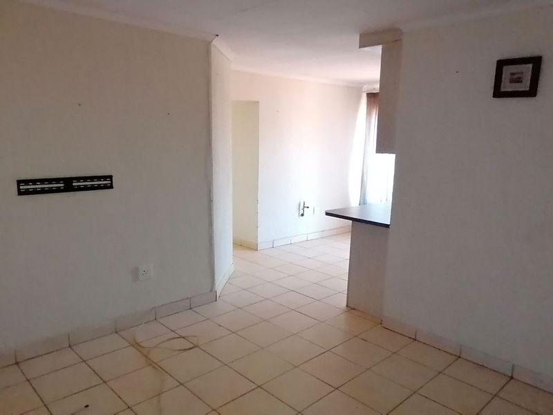 An empty open-plan living area featuring tiled flooring and a breakfast counter, providing a blank canvas for interior design.