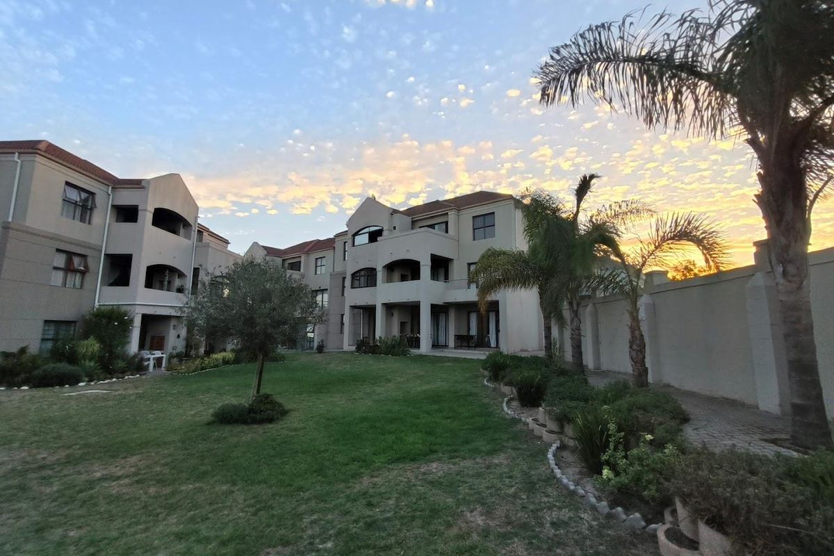 A view of the apartment complex rear elevation featuring landscaped gardens, manicured lawns, and private balconies under a sunset sky.