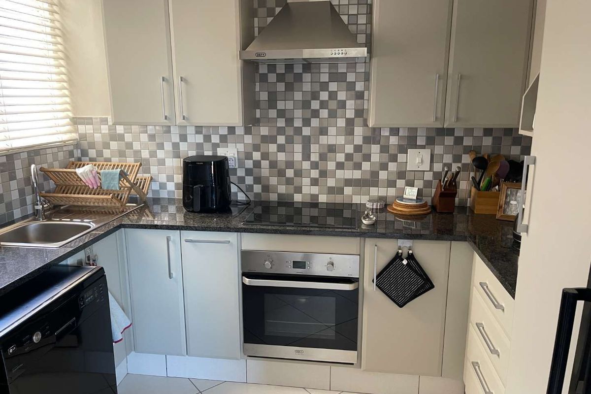A functional kitchen featuring granite countertops, a built-in oven, glass hob, stainless steel extractor fan, and tiled splashback.