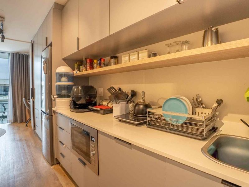 Modern galley-style kitchen featuring sleek built-in cabinetry, stone countertops, integrated microwave, and open shelving, leading to a bright balcony area.