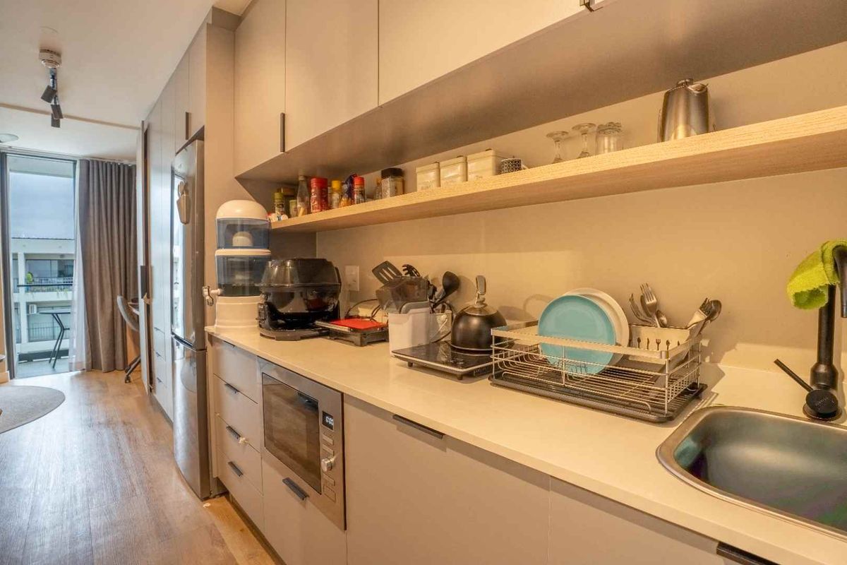 Modern galley-style kitchen featuring sleek built-in cabinetry, stone countertops, integrated microwave, and open shelving, leading to a bright balcony area.