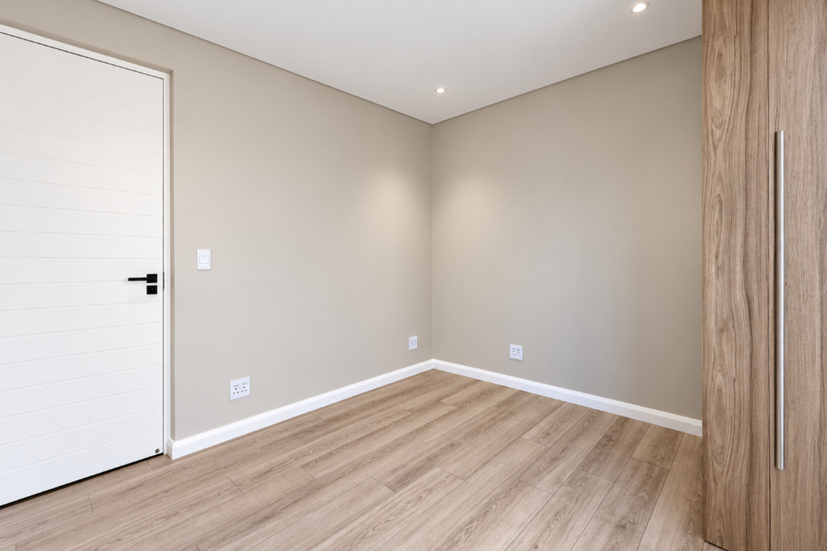 A bright, modern bedroom featuring light wood-look laminate flooring, neutral walls, recessed ceiling lighting, and a sleek built-in wardrobe with a tall handle.