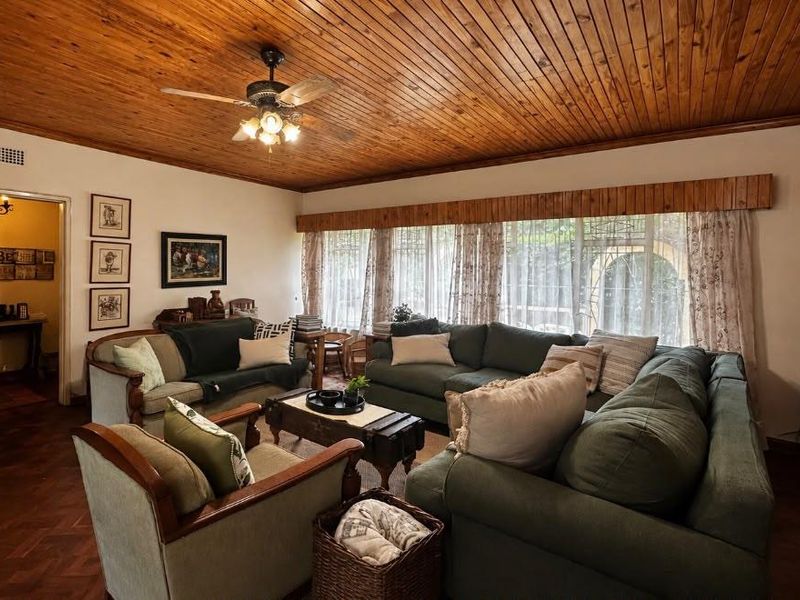 A cozy living room featuring warm timber ceilings, classic parquet flooring, and large windows with security bars, offering a traditional and inviting atmosphere.