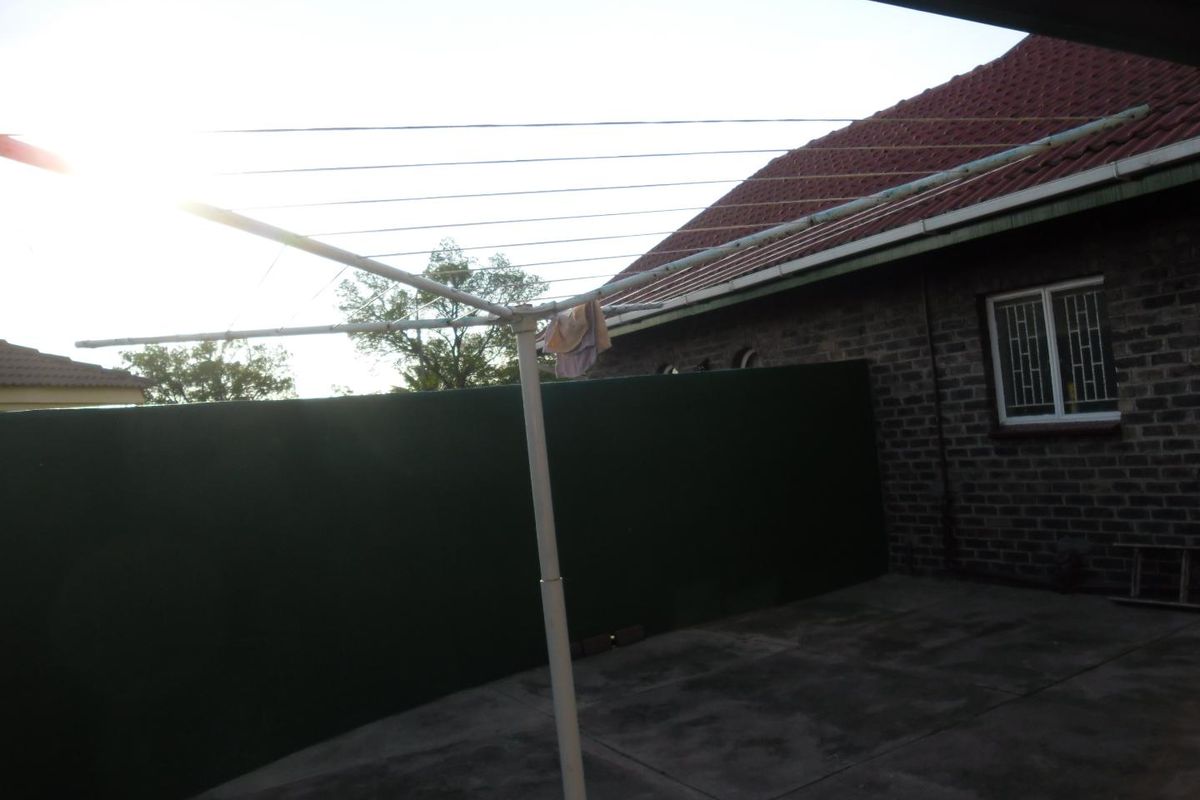 Rear exterior area featuring a paved patio, brick wall construction, tiled roof, and a rotary clothesline.