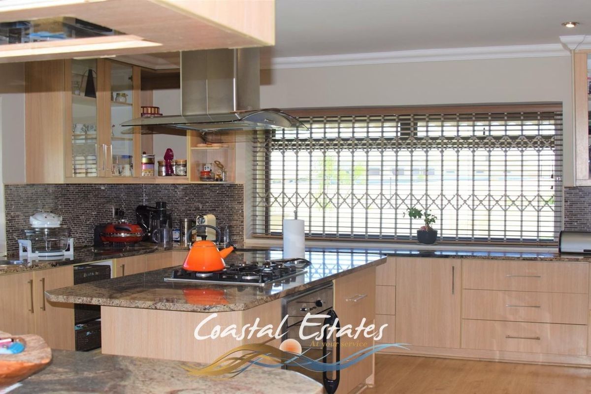 Modern kitchen featuring light wood cabinetry, granite countertops, a central island with a built-in gas hob, and a stainless steel extractor fan.